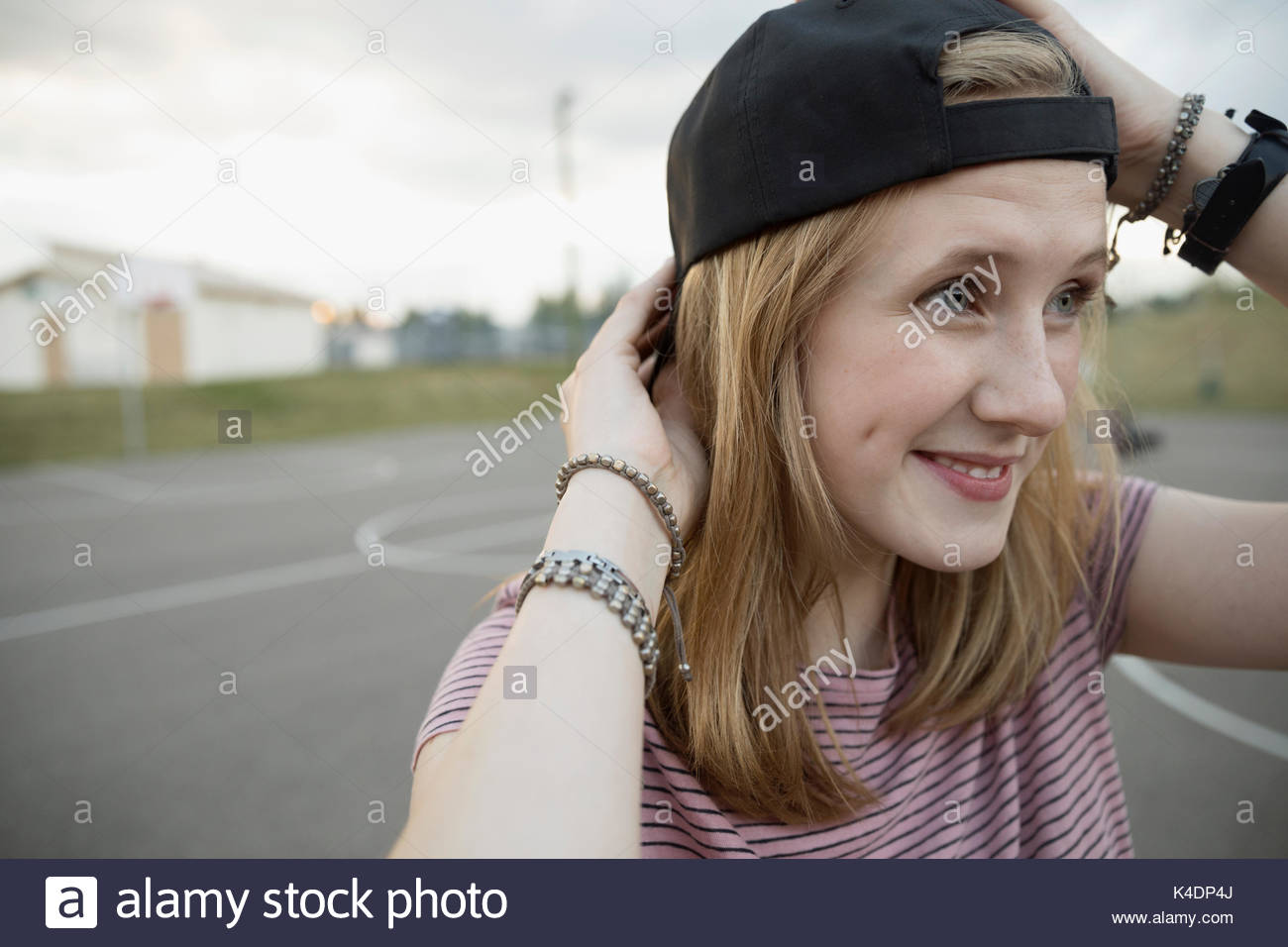 Smiling teenage girl wearing backward baseball cap on outdoor basketball court Stock Photo