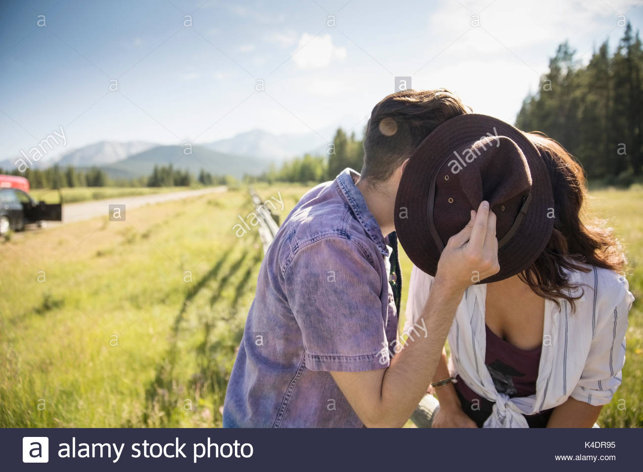 Affectionate young couple kissing behind hat in sunny summer rural grass Stock Photo