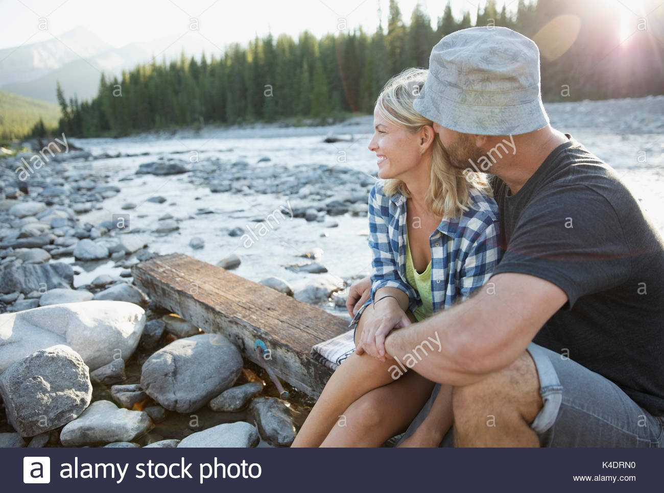 Affectionate couple sitting on wood plank along summer stream Stock Photo
