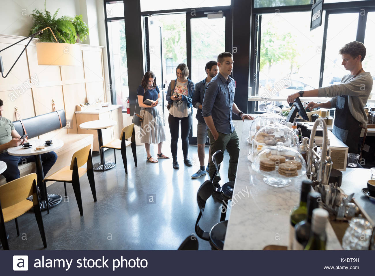 Male worker helping customers in queue at cafe counter Stock Photo
