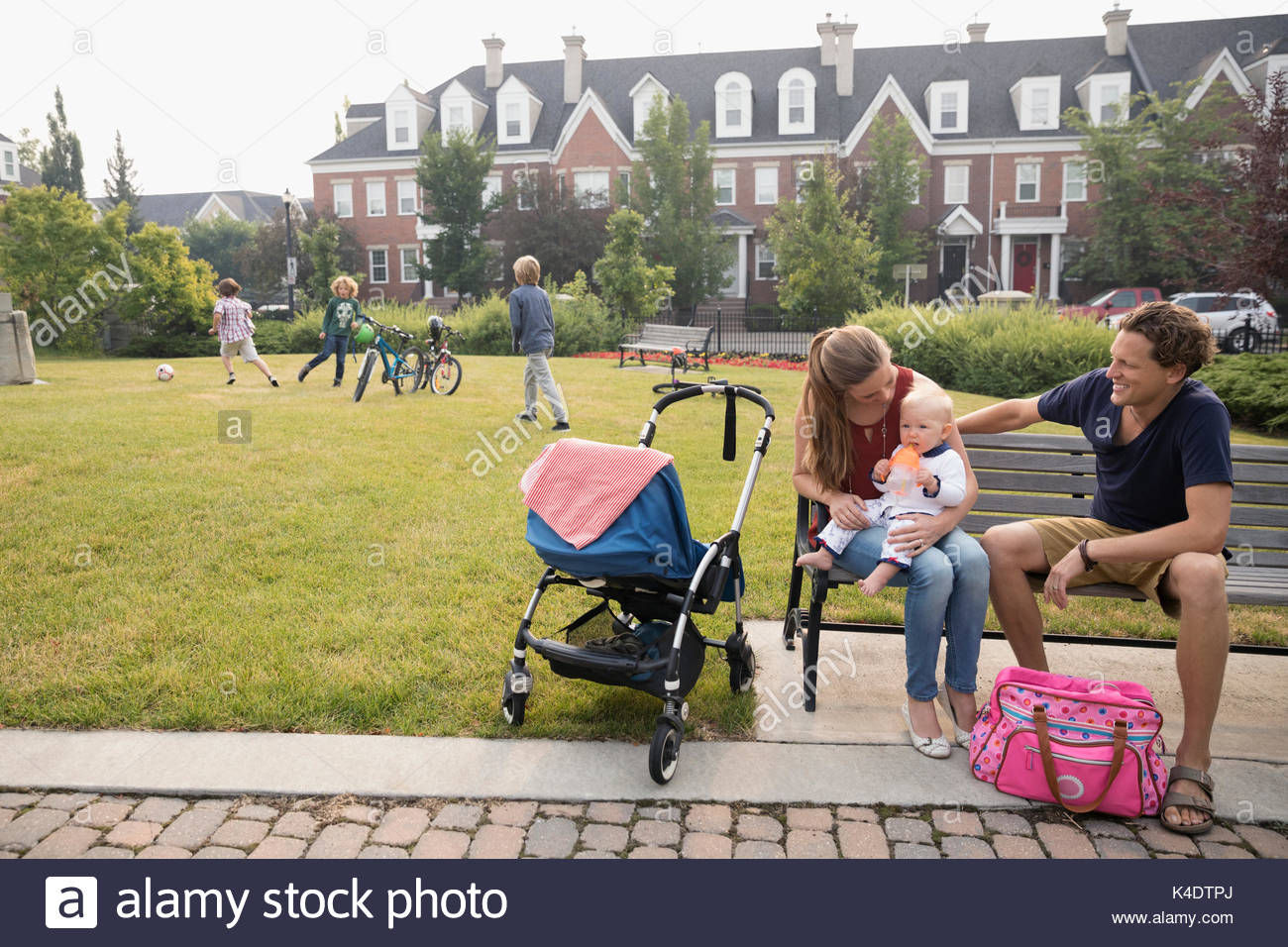Young family with baby sitting on neighborhood park bench Stock Photo