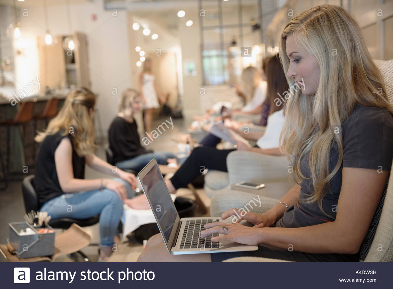 Woman getting pedicure and working at laptop in nail salon Stock Photo