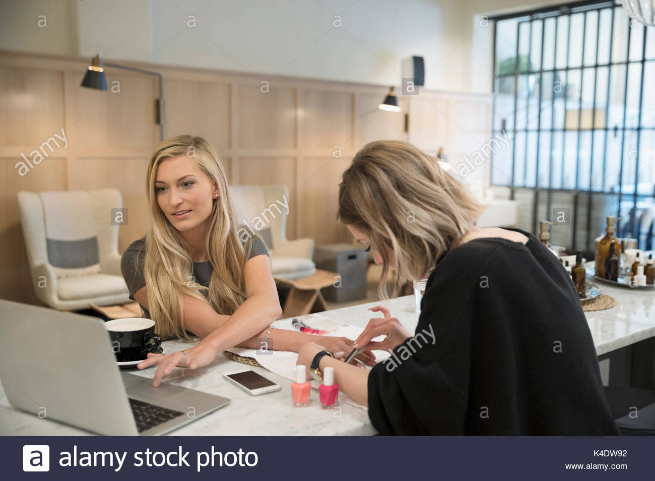 Female nail technician giving manicure to customer using laptop in nail salon Stock Photo