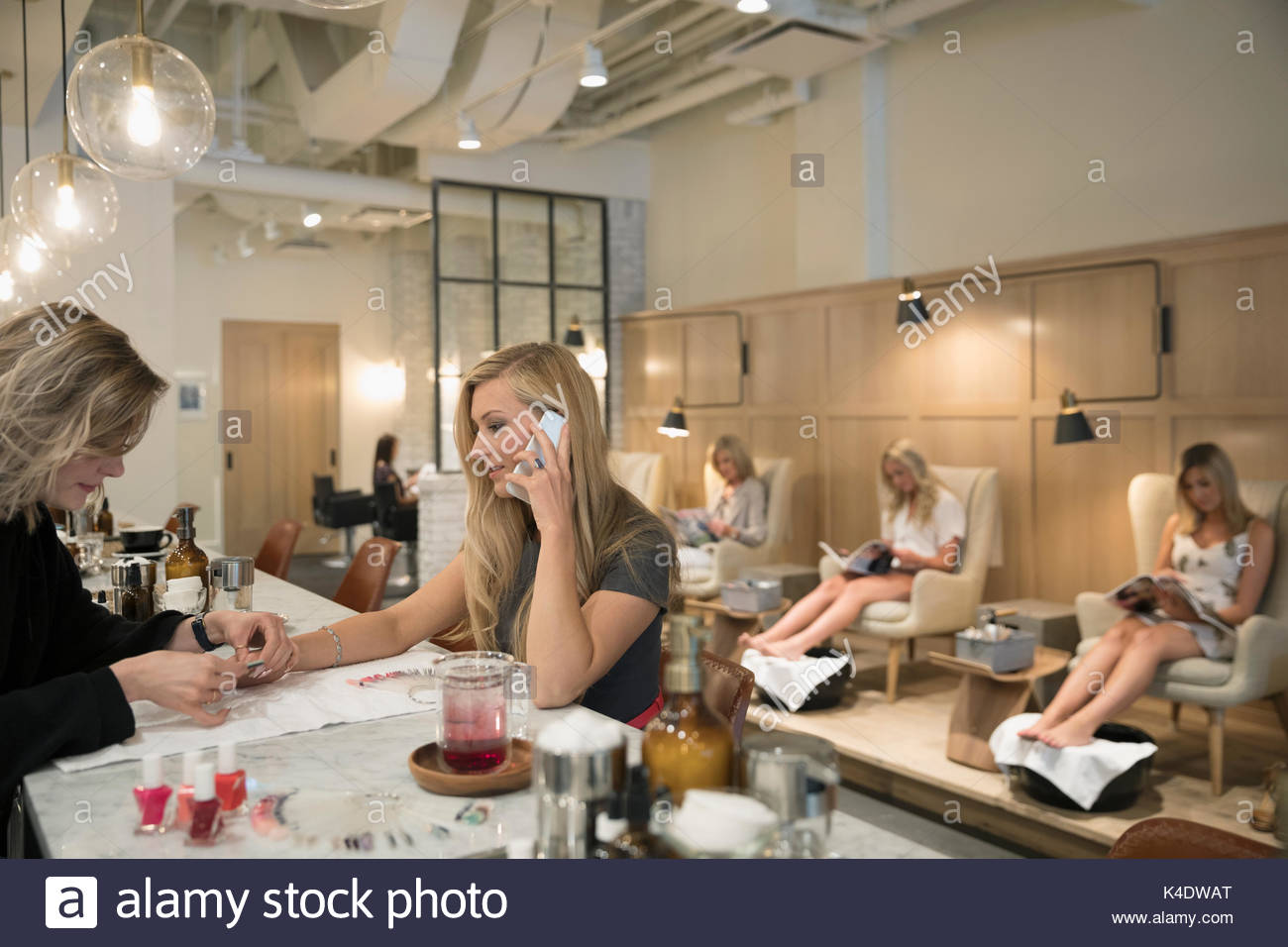 Female nail technician giving manicure to customer talking on cell phone in nail salon Stock Photo