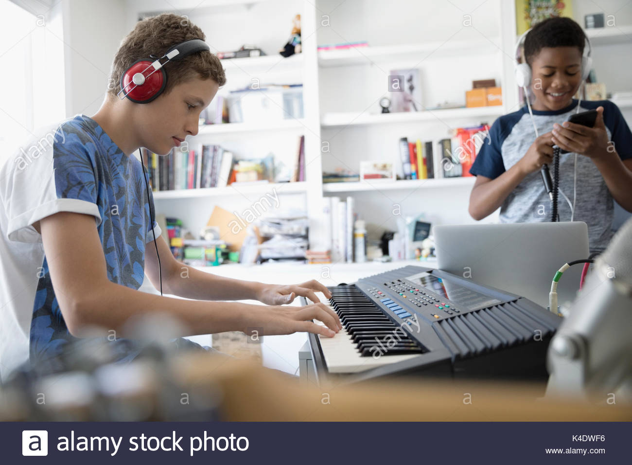 Teenage boy with headphones playing keyboard piano in home office Stock