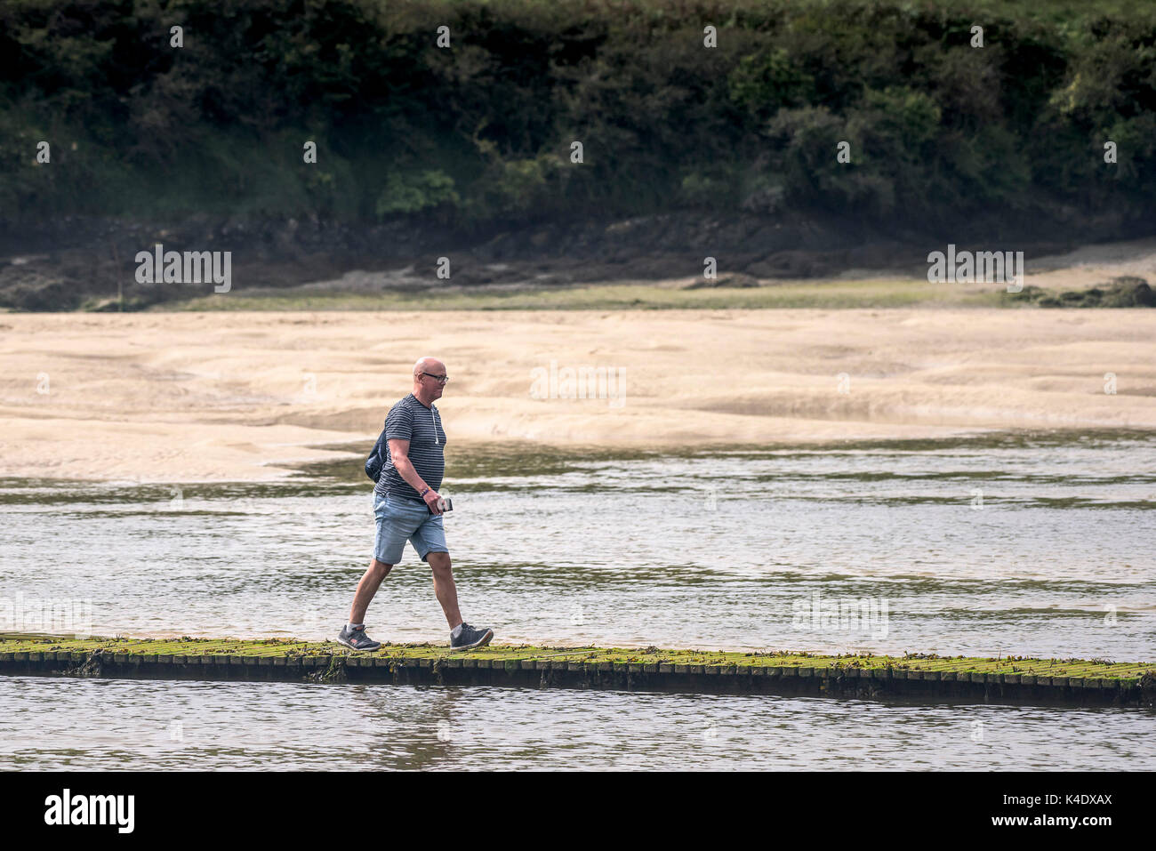 Gannel Estuary - a lone man walking across a footbridge at low tide on the Gannel River in Newquay, Cornwall. Stock Photo