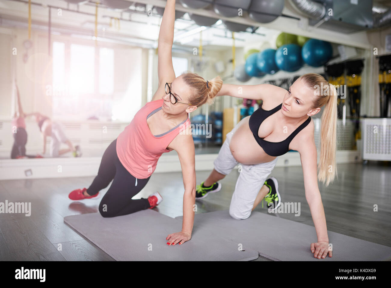Side portrait of pregnant woman exercising with personal trainer Stock Photo