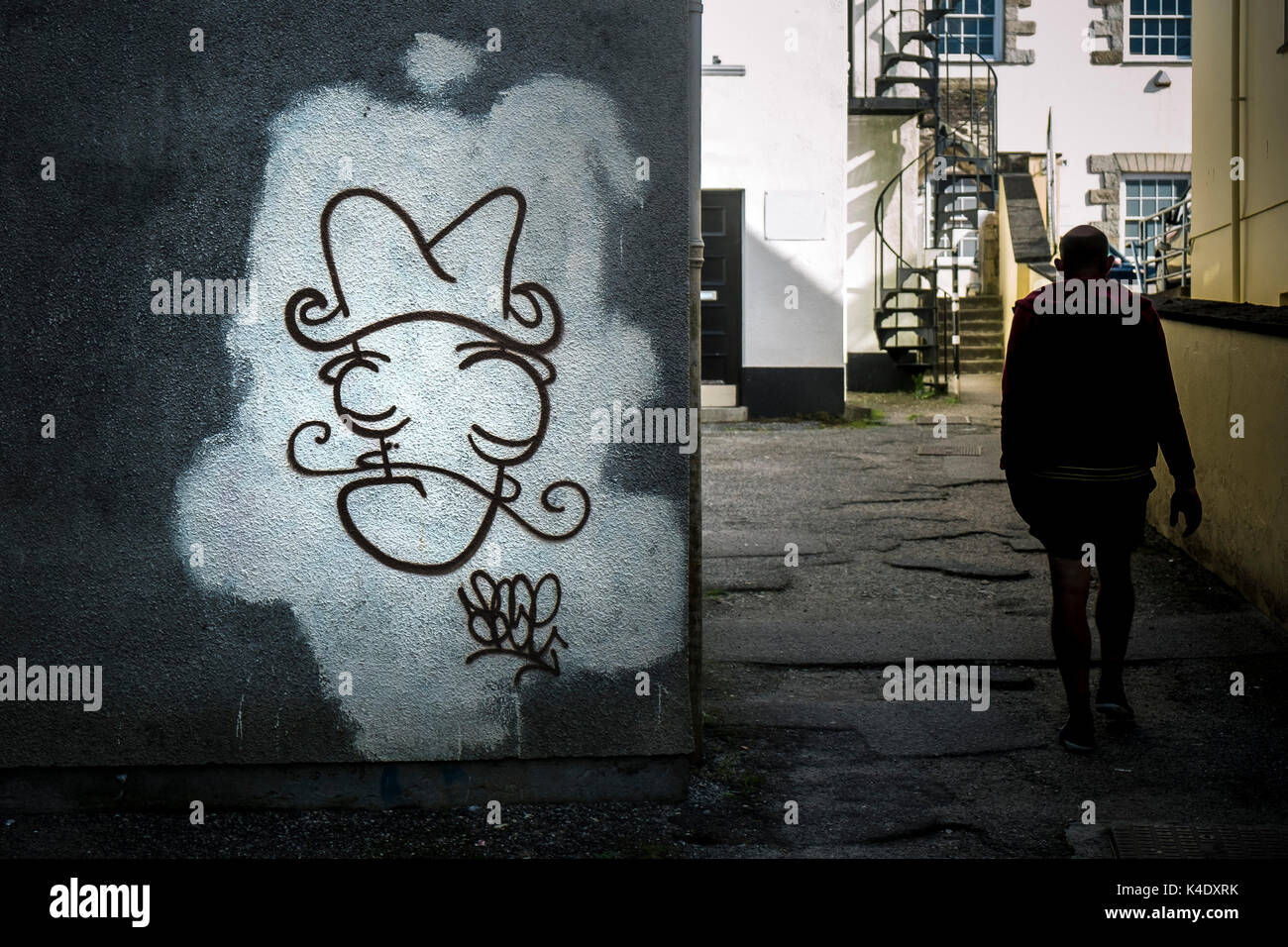 Graffiti - A figure walking past graffiti sprayed on a wall in Truro City centre in Cornwall. Stock Photo