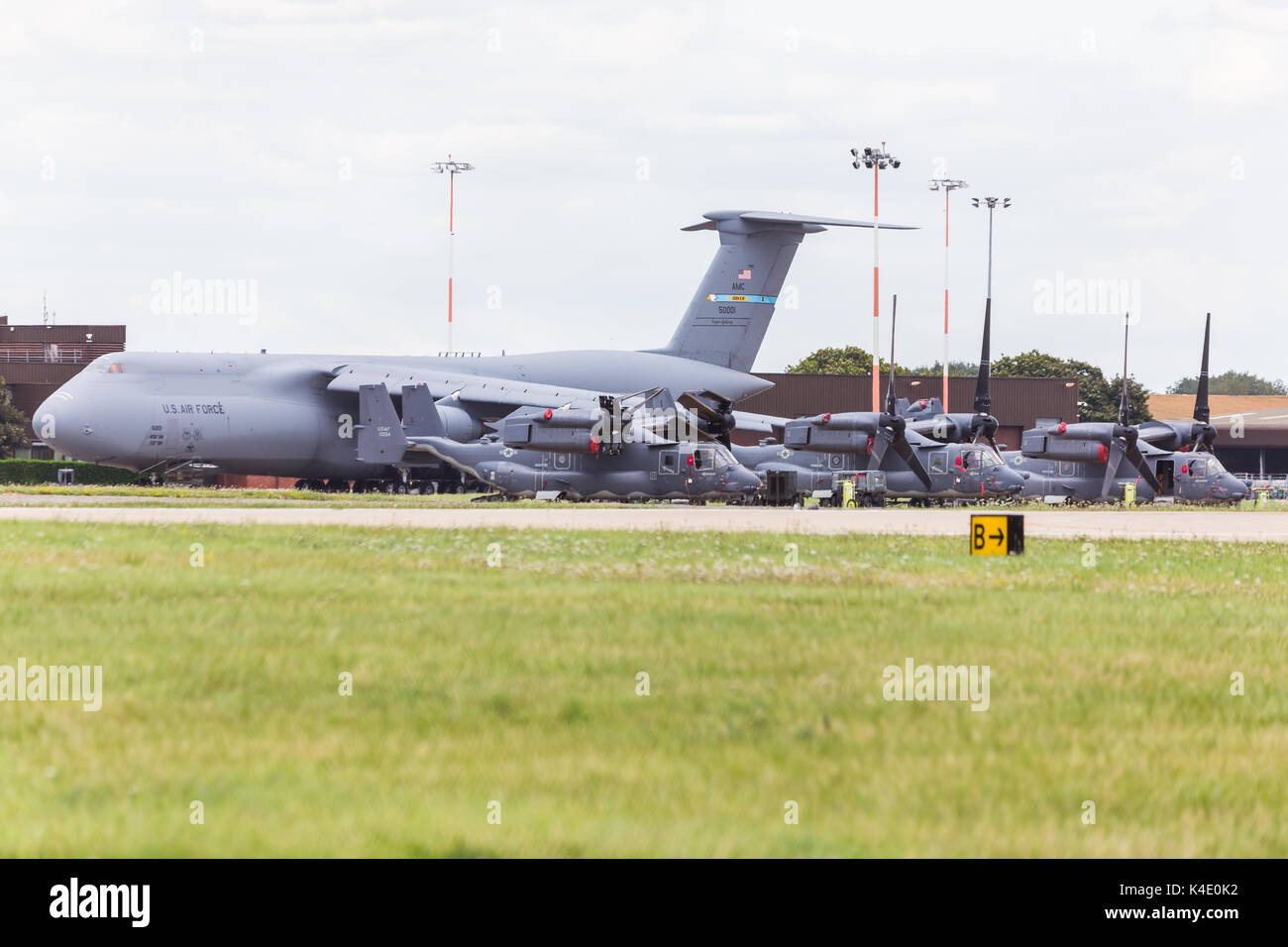 A massive C-5M Super Galaxy transport aircraft seen on the ground at RAF Mildenhall behind three CV-22 Ospreys. Stock Photo