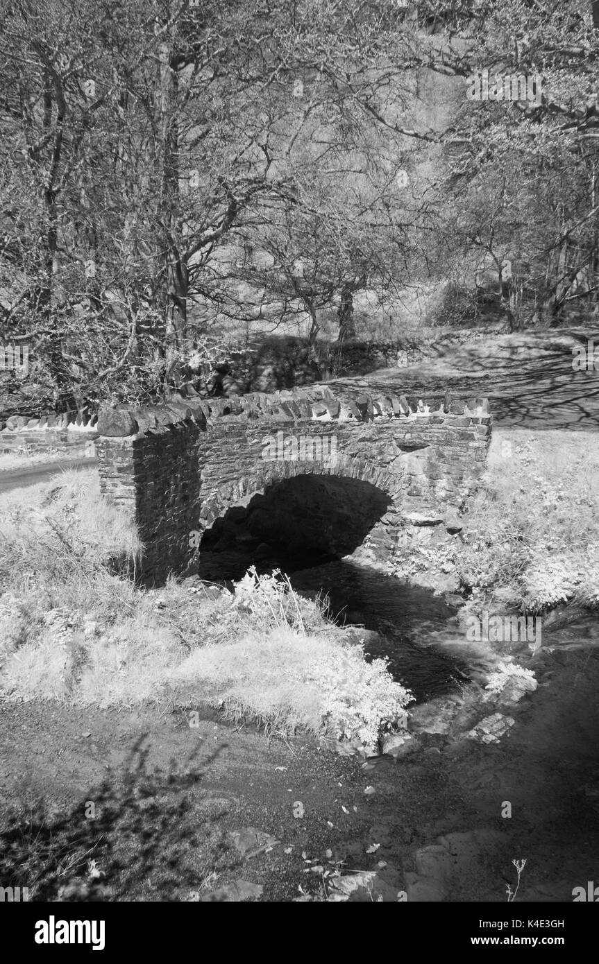 Infrared picture of the ancient granite built Robbers Bridge over Weir Water near Oareford in Somerset part of Exmoor National Park Stock Photo