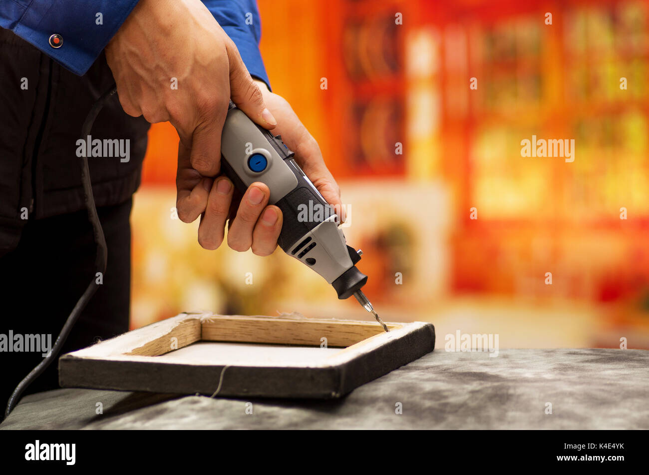Closeup of a hardworker man drilling a wooden frame with his drill, with drilling accessories over a gray table in a blurred background Stock Photo