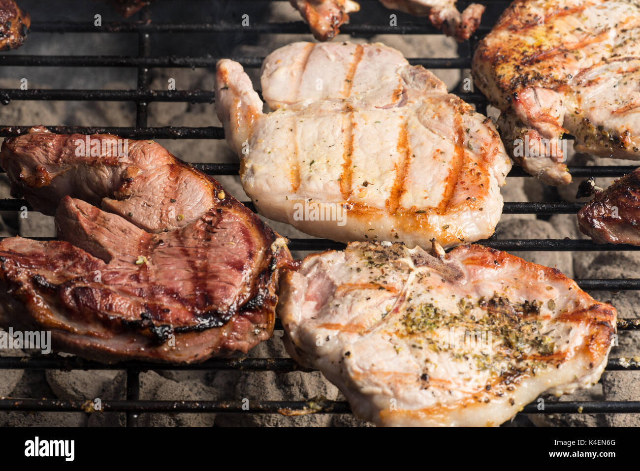 Seasoned pork chops and lamb steak cooking on the charcoal bbq grill