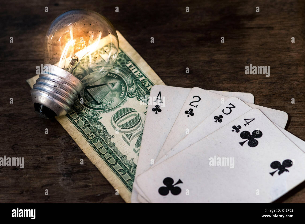 Lit light bulb, US money one dollar bill and white playing cards, face up, on top of a wooden surface, money, gambling and winning concept idea Stock Photo