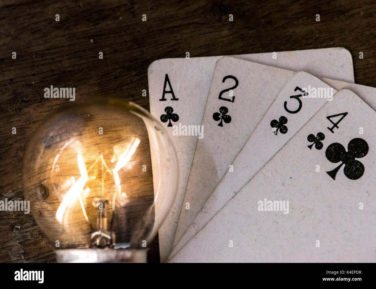 Lit light bulb and white playing cards, face up, on top of a wooden surface, gambling and winning concept idea Stock Photo