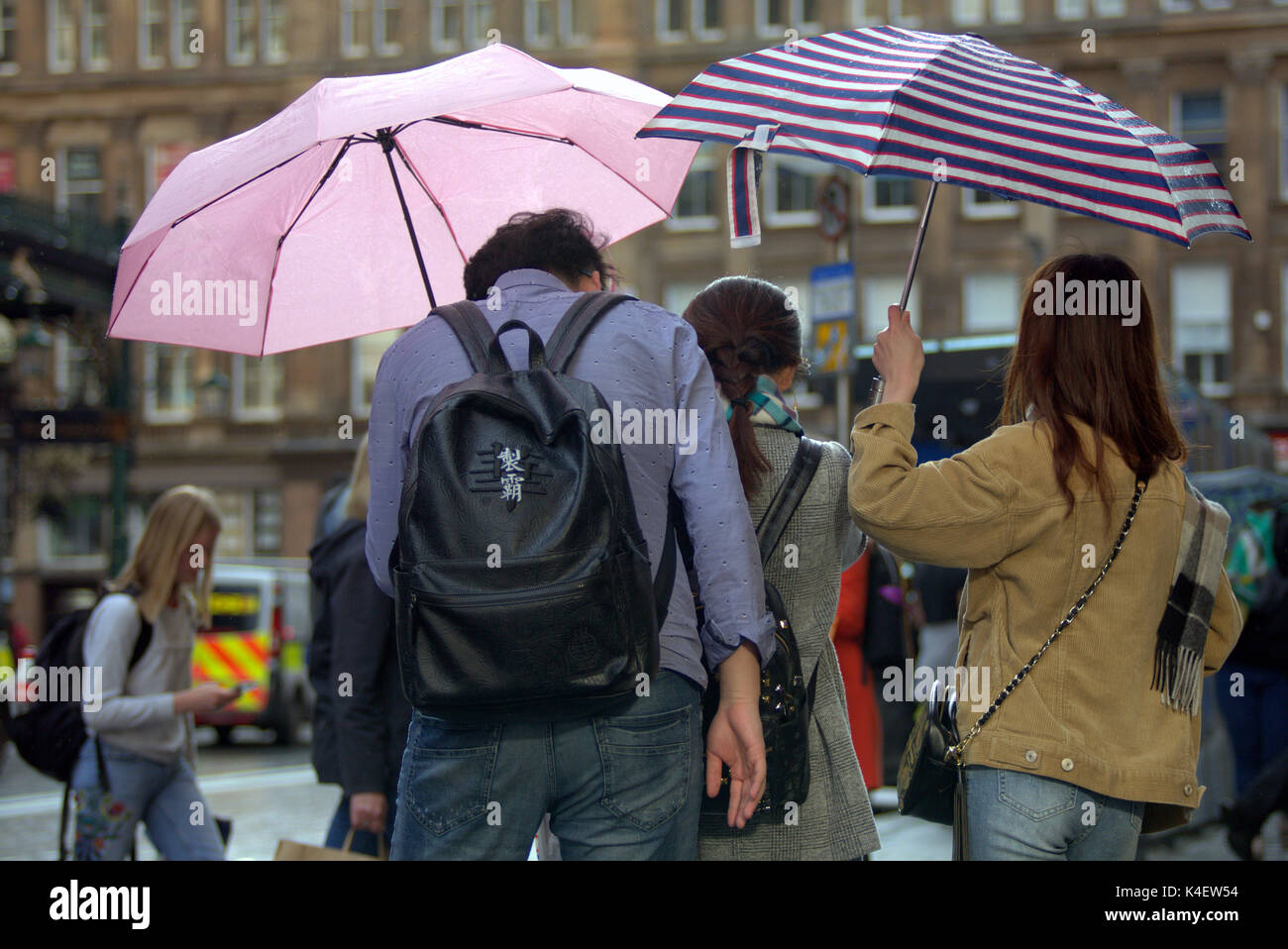 Glasgow street scene Chinese tourists looking at smartphone pictures in the rain from Behind Stock Photo
