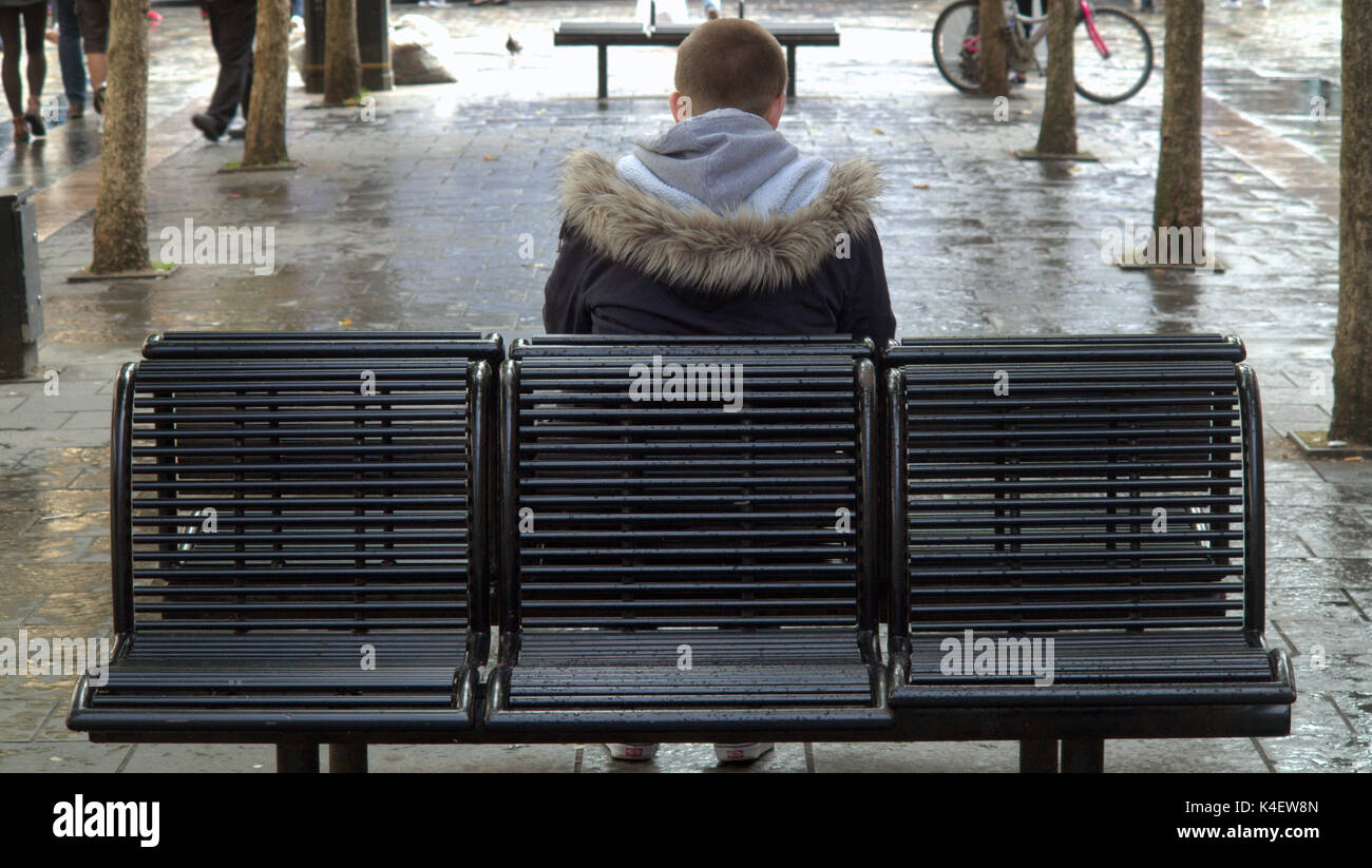 Glasgow street scene young man sitting on bench alone distressed from behind Stock Photo