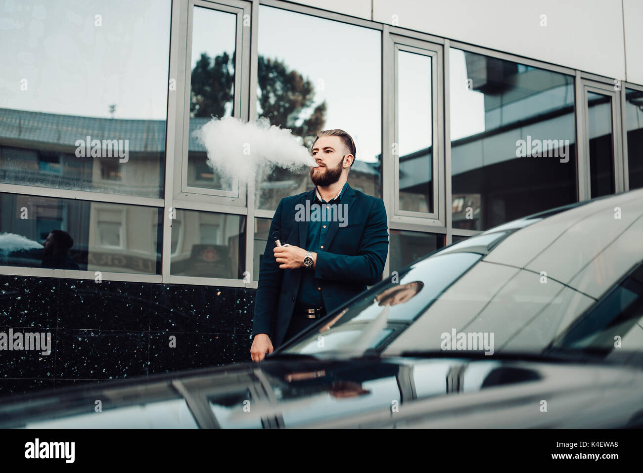 bearded man in a suit in the city vaping Stock Photo