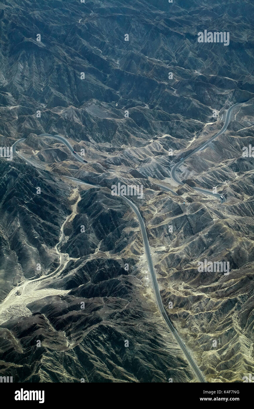 Pan-American Highway winds it's way through eroded hills in the desert south of Ica, Peru, South America - aerial Stock Photo