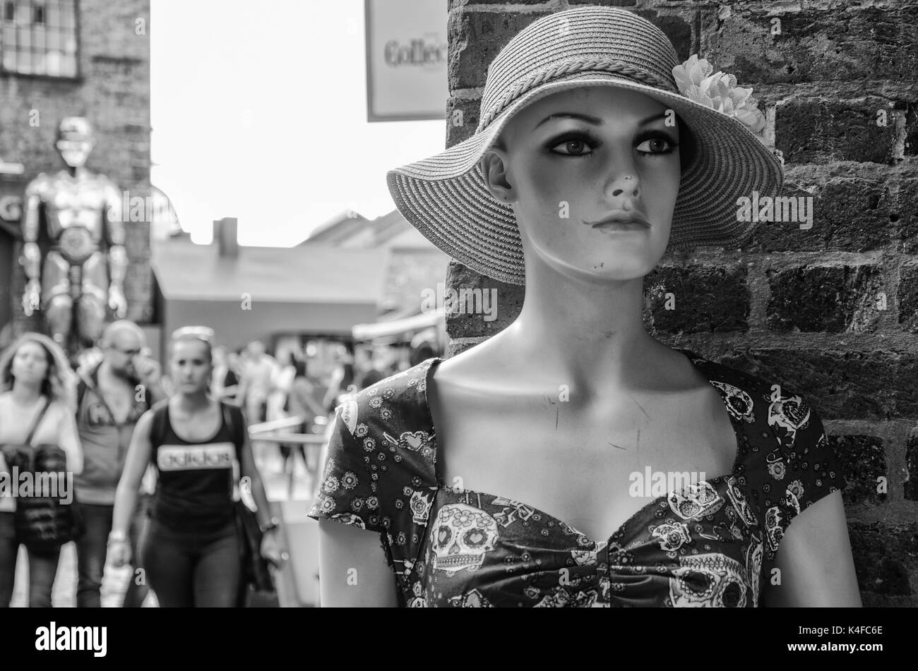 A shop mannequin stands in-front of a brick wall. People in the background are out of focus. Stock Photo