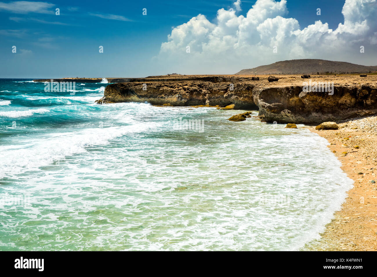 Sunny summer day with blue sky on the eastern shore of Aruba. Foamy waves splash the rocky beach. Stock Photo
