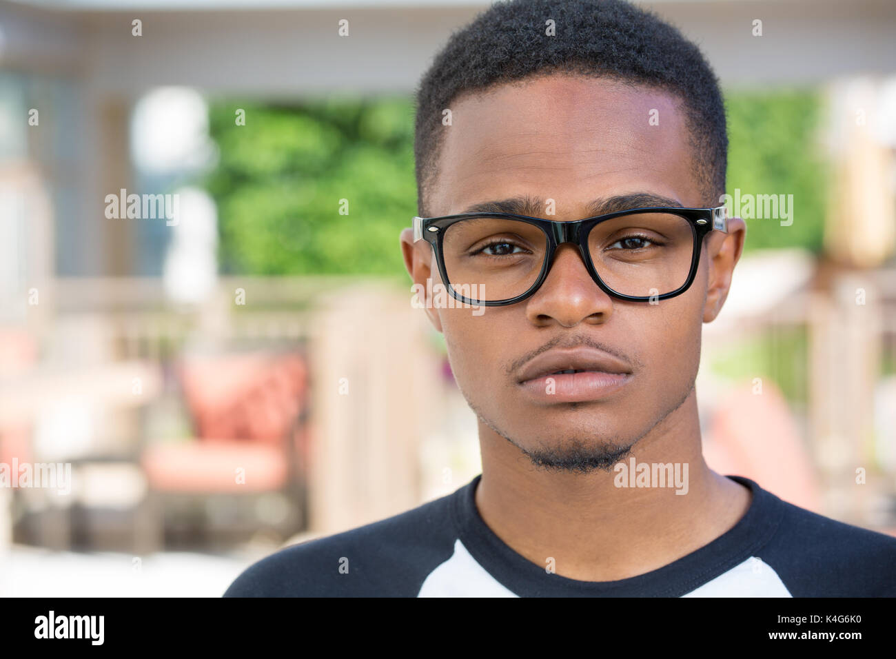 Closeup headshot portrait of fine young man with big glasses, undergrad student, straight face, isolated on outside outdoors background. Stock Photo
