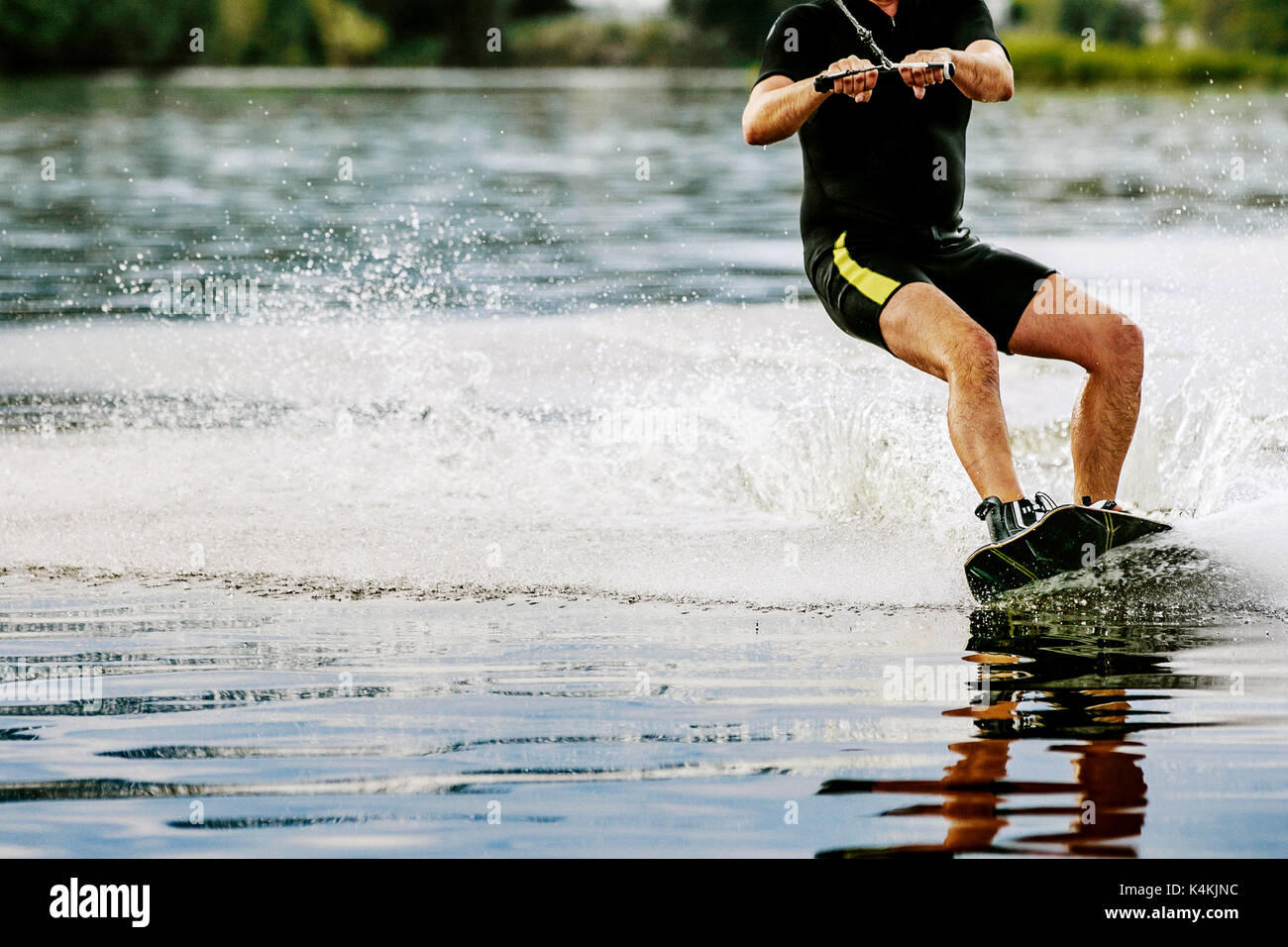 male wakeboarder rides on lake in wakeboard splashes of water Stock Photo