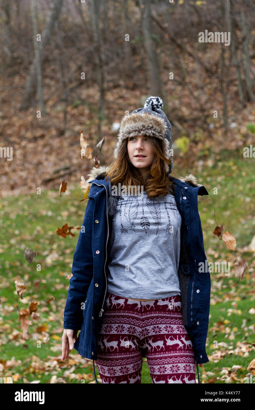 Close up of a young woman wearing winter hat surrounded by leaves. Soft focus Stock Photo