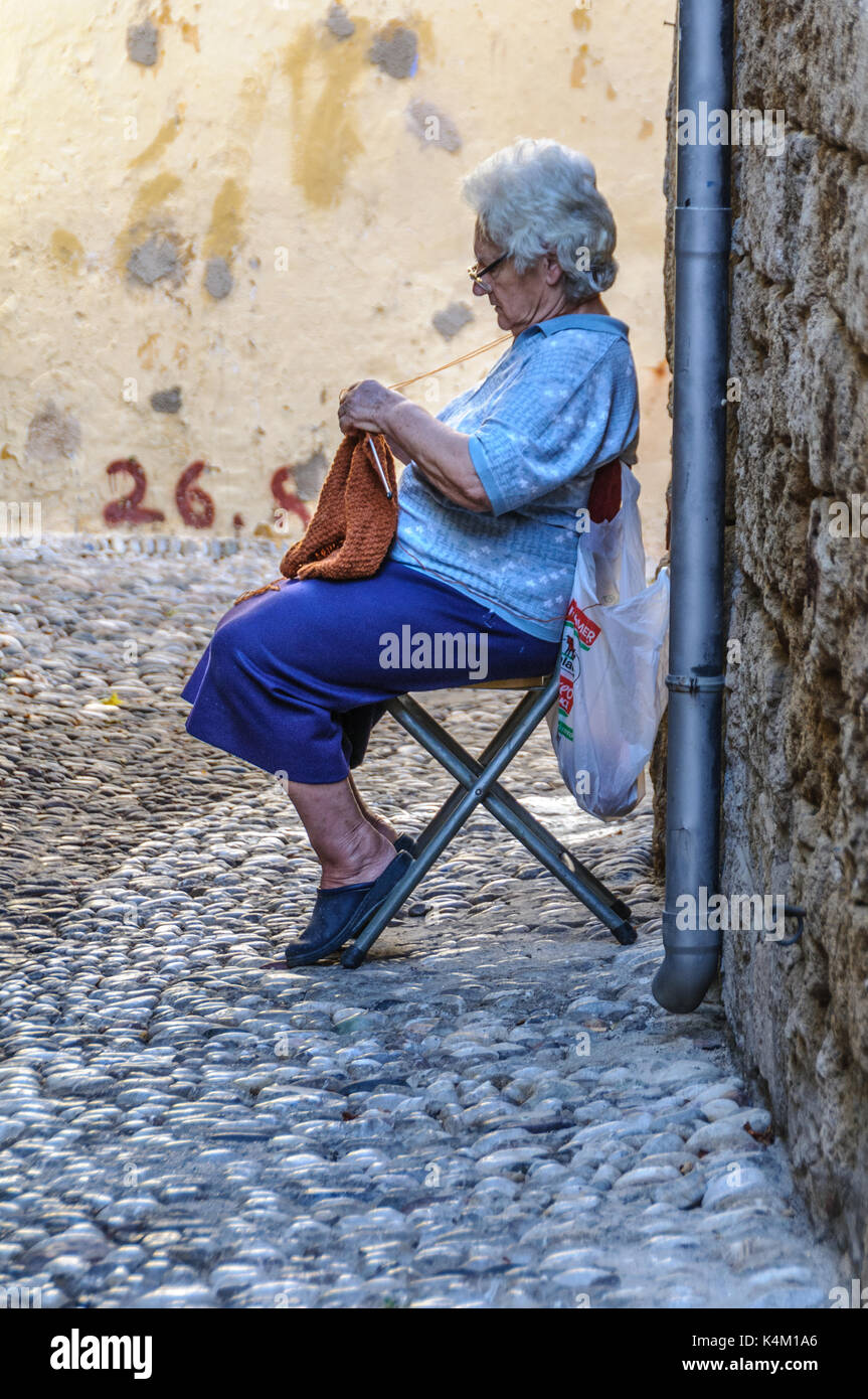 Old Lady Sitting Knitting at Streetside in Rhodes Old Town, Greece. Stock Photo