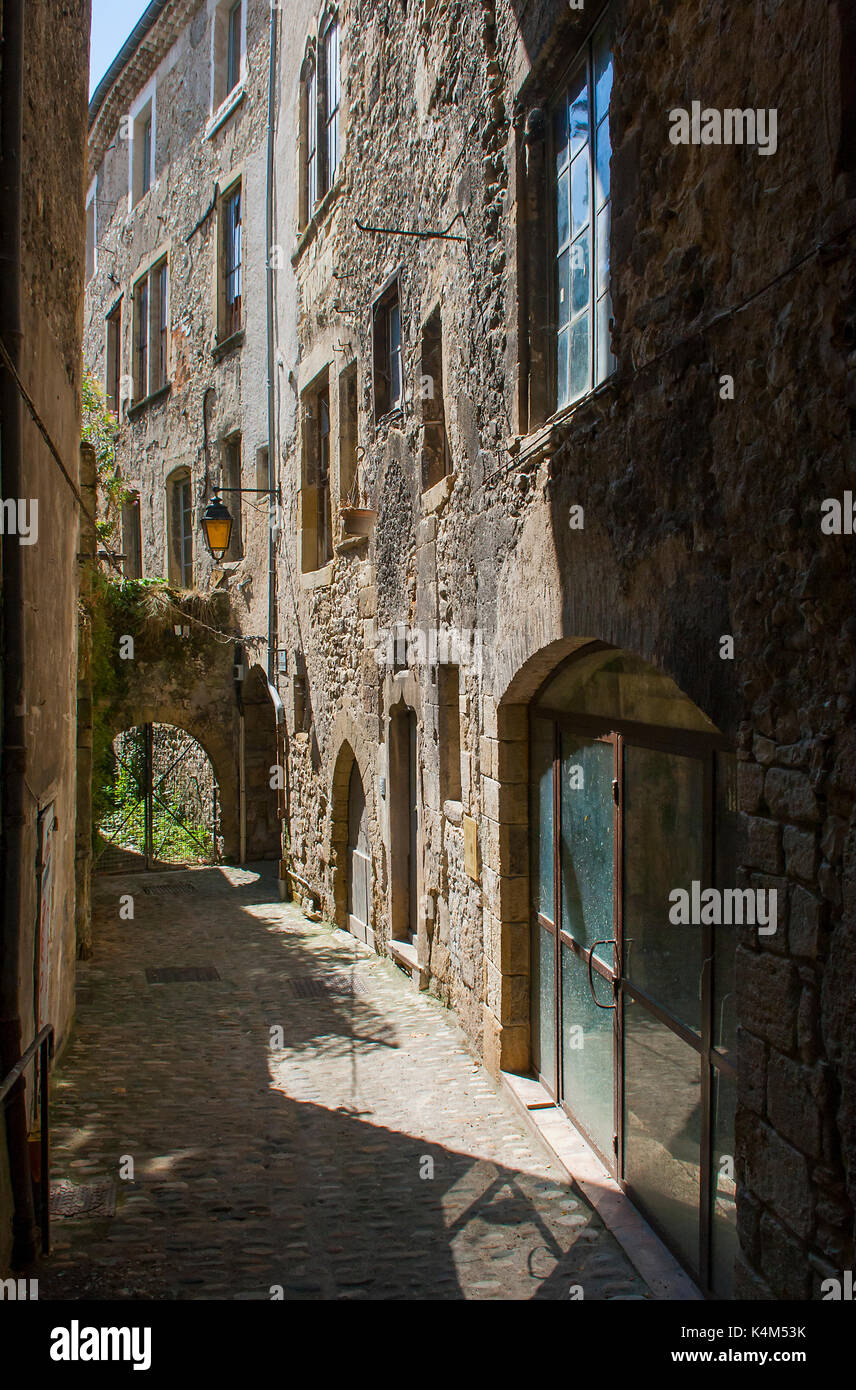 A typical narrow alleyway in the city of Montelimar in France with tall stone buildings and doorways with dark shadows Stock Photo