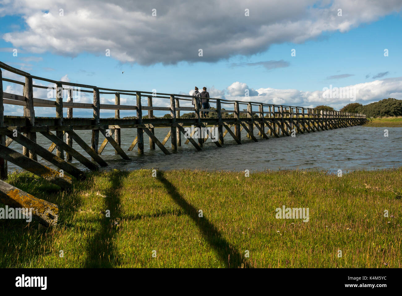 Young couple walking on wooden footbridge over mudflats at high tide at Aberlady Bay local nature reserve, East Lothian, Scotland, UK Stock Photo