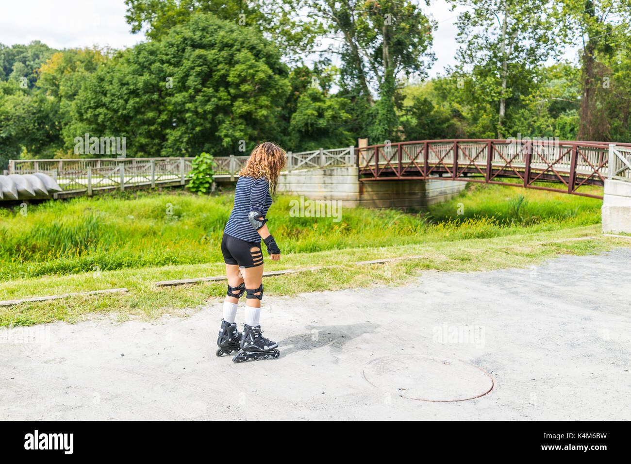 Young woman learning rollerblading outside outdoor in summer park with knee and elbow pads by bridge Stock Photo