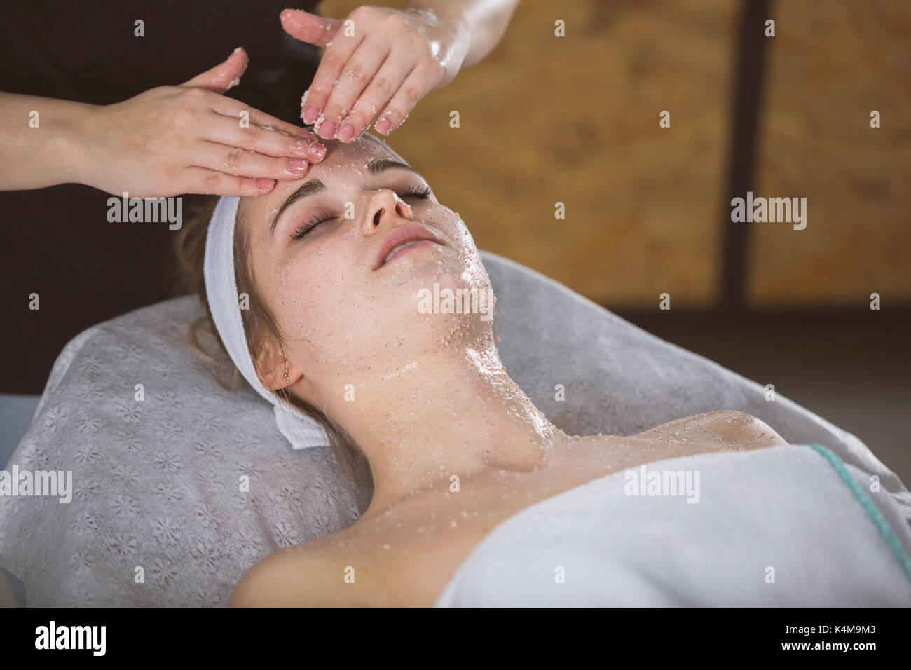 Beautician applying exfoliating salt scrub on woman's face Stock Photo