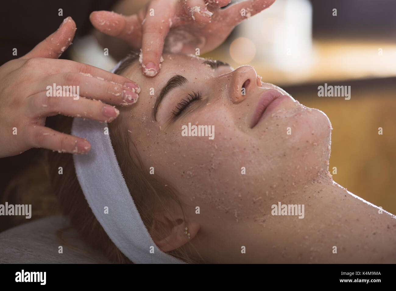 Beautician applying exfoliating salt scrub on woman's face Stock Photo