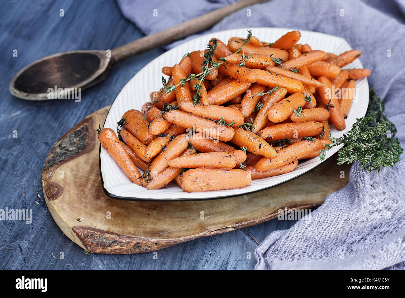 Honey Glazed Baby carrots with an old rustic wooden spoon and thyme. Extreme shallow depth of field with selective focus on carrots in the foreground. Stock Photo