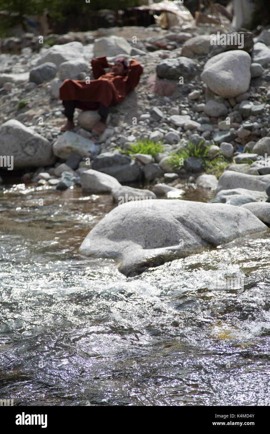 Berber man relaxes by river during souk of Setti Fatma, Ourika Valley, Atlas Mountains, Morocco Stock Photo