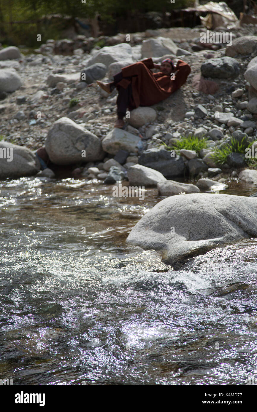 Berber man relaxes by river during souk of Setti Fatma, Ourika Valley, Atlas Mountains, Morocco Stock Photo