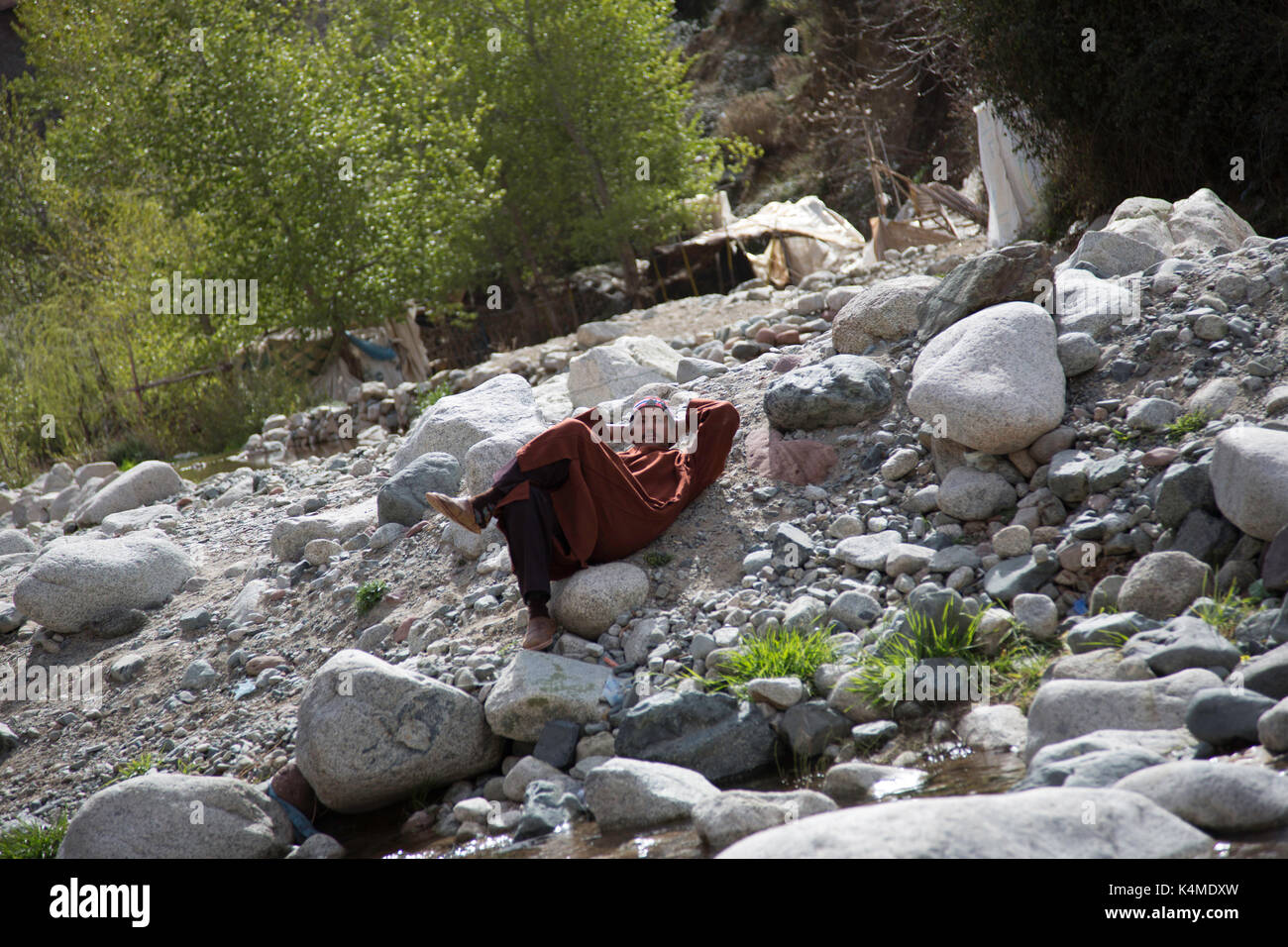 Berber man relaxes by river during souk of Setti Fatma, Ourika Valley, Atlas Mountains, Morocco Stock Photo