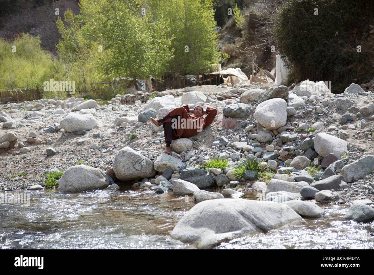 Berber man relaxes by river during souk of Setti Fatma, Ourika Valley, Atlas Mountains, Morocco Stock Photo