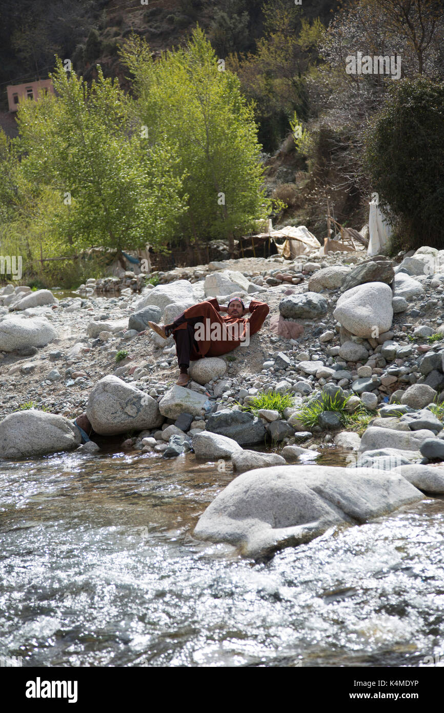 Berber man relaxes by river during souk of Setti Fatma, Ourika Valley, Atlas Mountains, Morocco Stock Photo