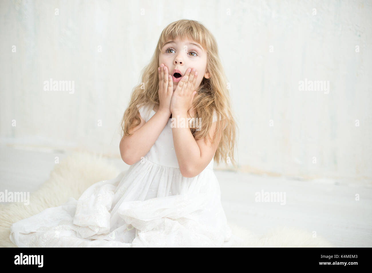 Portrait of pretty little girl in white dress , she is surprised and ...