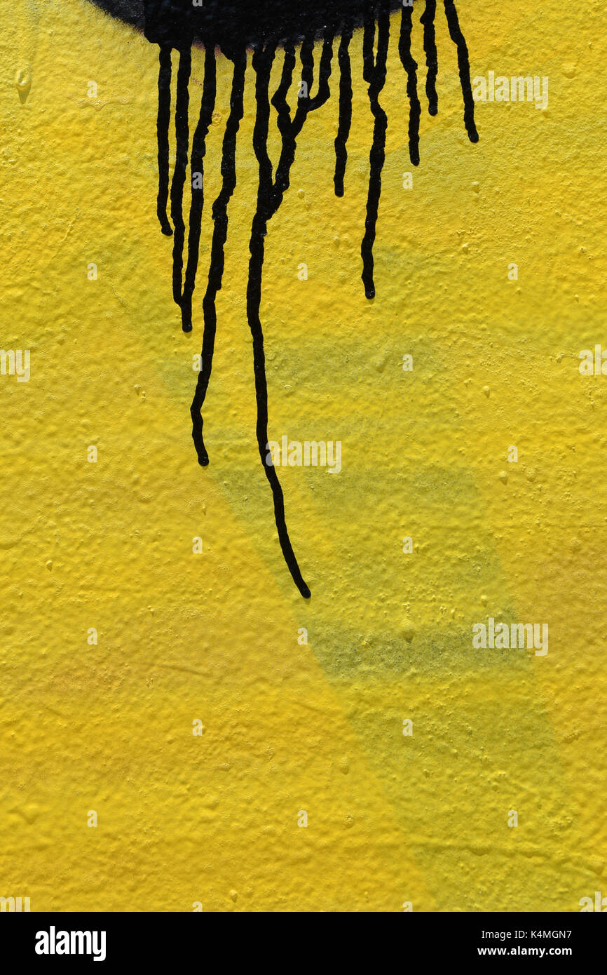 Black color dripping on yellow paint smudged wall background. Abstract artistic texture. Stock Photo