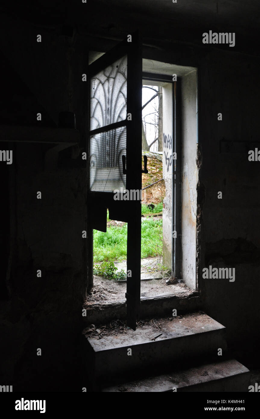Dark abandoned house interior dirty steps and light through broken door with antique metalwork motif. Stock Photo