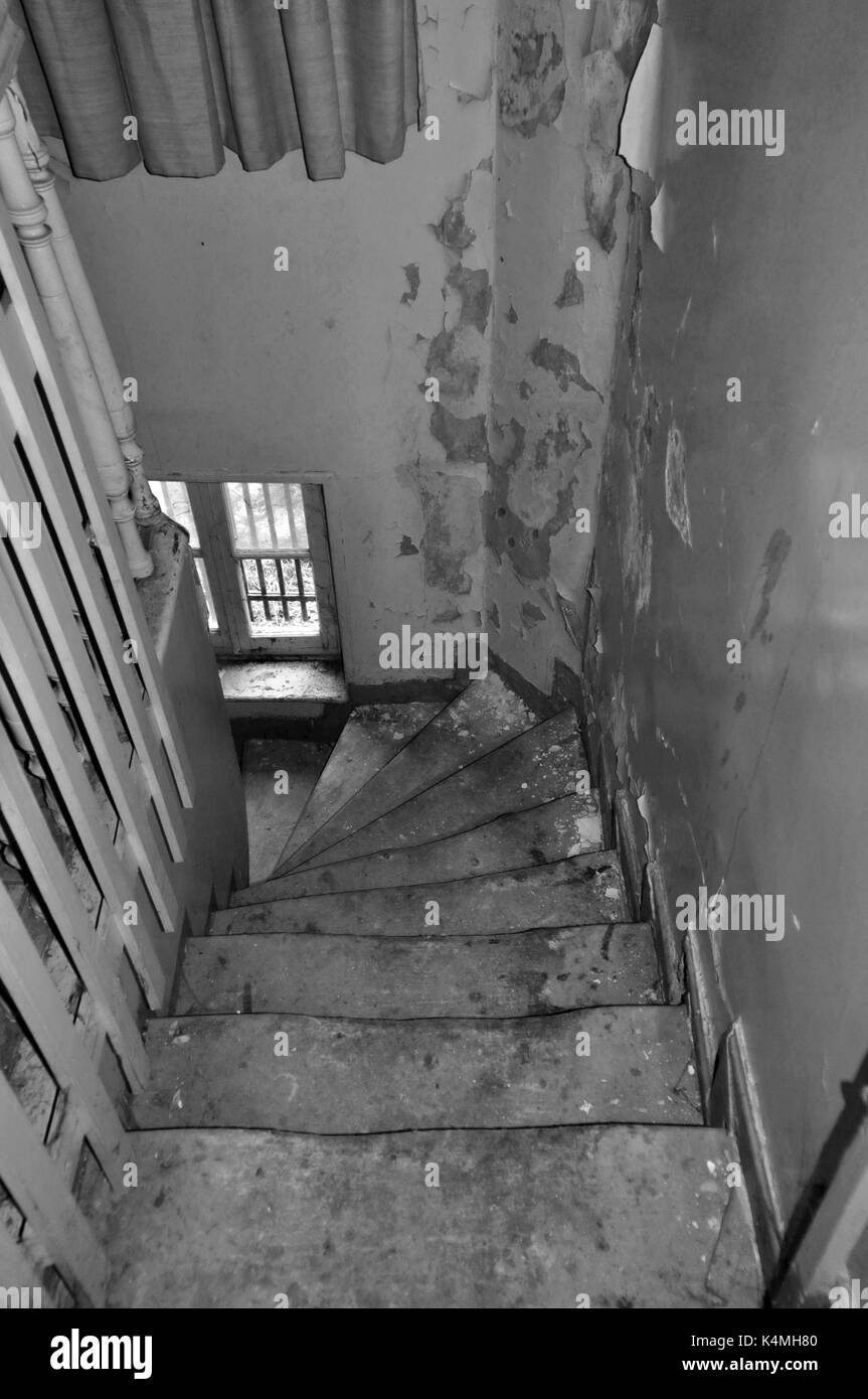 Crooked wooden staircase and peeling paint wall in abandoned house. Black and white. Stock Photo