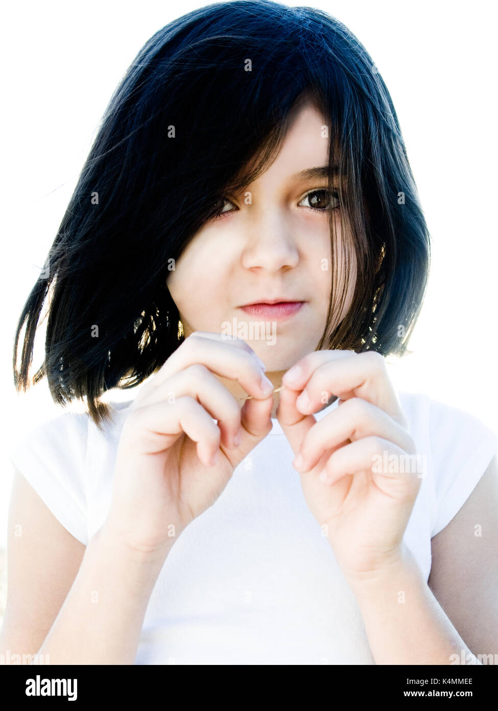 Portrait of a young girl, elementary school age, brightly lit outside for a high contrast effect. Looking at camera and being playful. Stock Photo