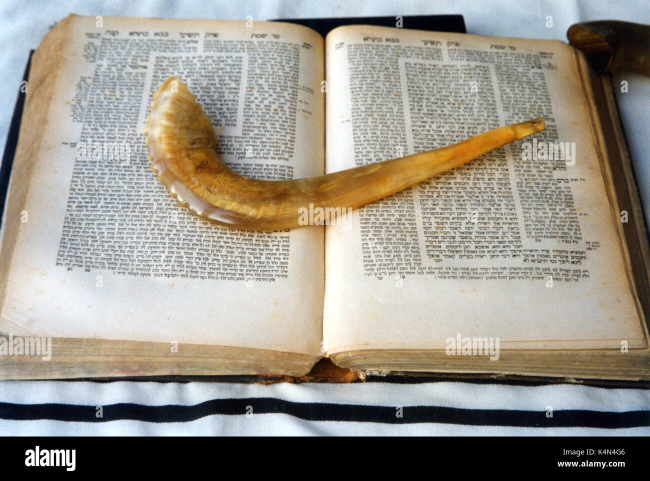 Shofar  (ram's horn) lying on an open copy of Talmud in Hebrew - rabbinic biblical commentary.  Underneath is a prayer shawl (talit) Stock Photo