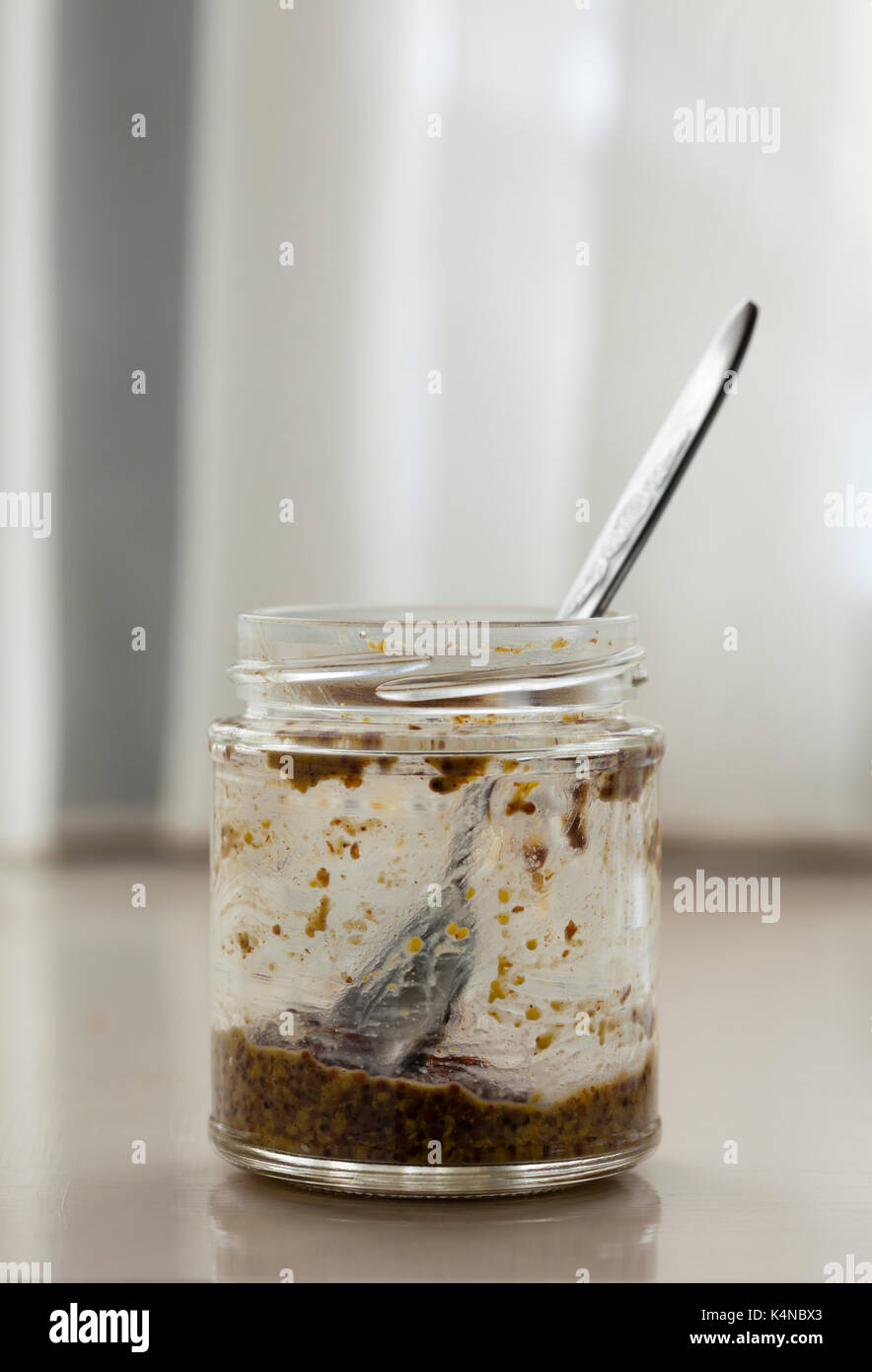 An almost empty jar of wholegrain mustard and teaspoon sticking out. Rather than going to waste, what's left can be turned into a salad dressing. Stock Photo