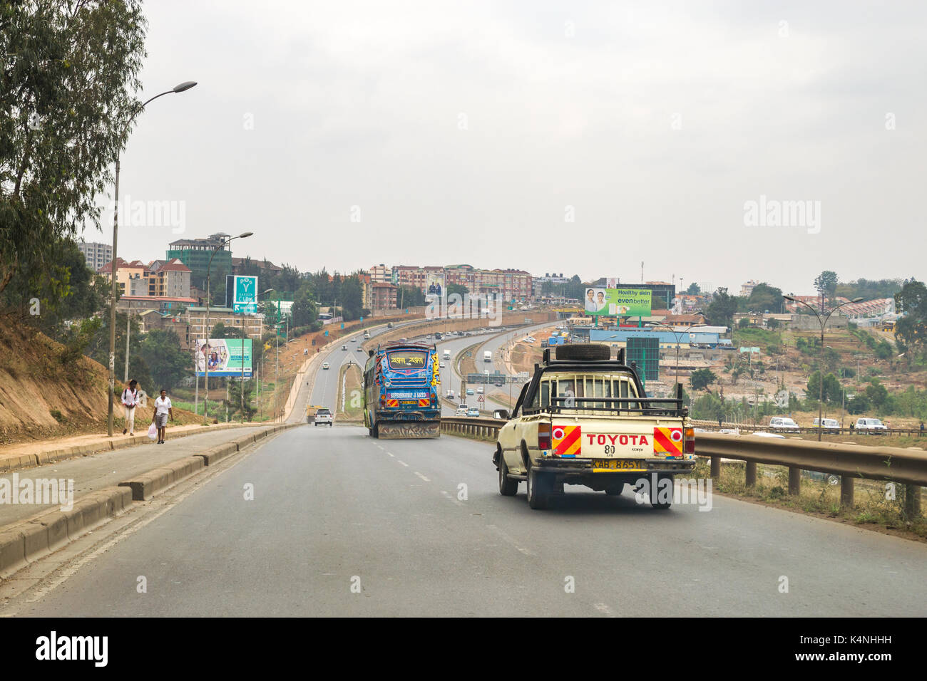Vehicles driving on slip road to Thika Highway with traffic on main highway as pedestrians walk on side of road, Nairobi, Kenya Stock Photo