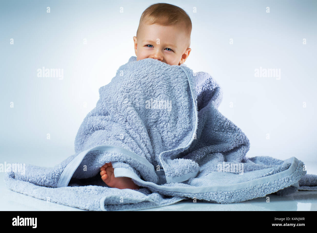 Eight month baby after washing sitting in big soft towel and smiling on white background Stock Photo