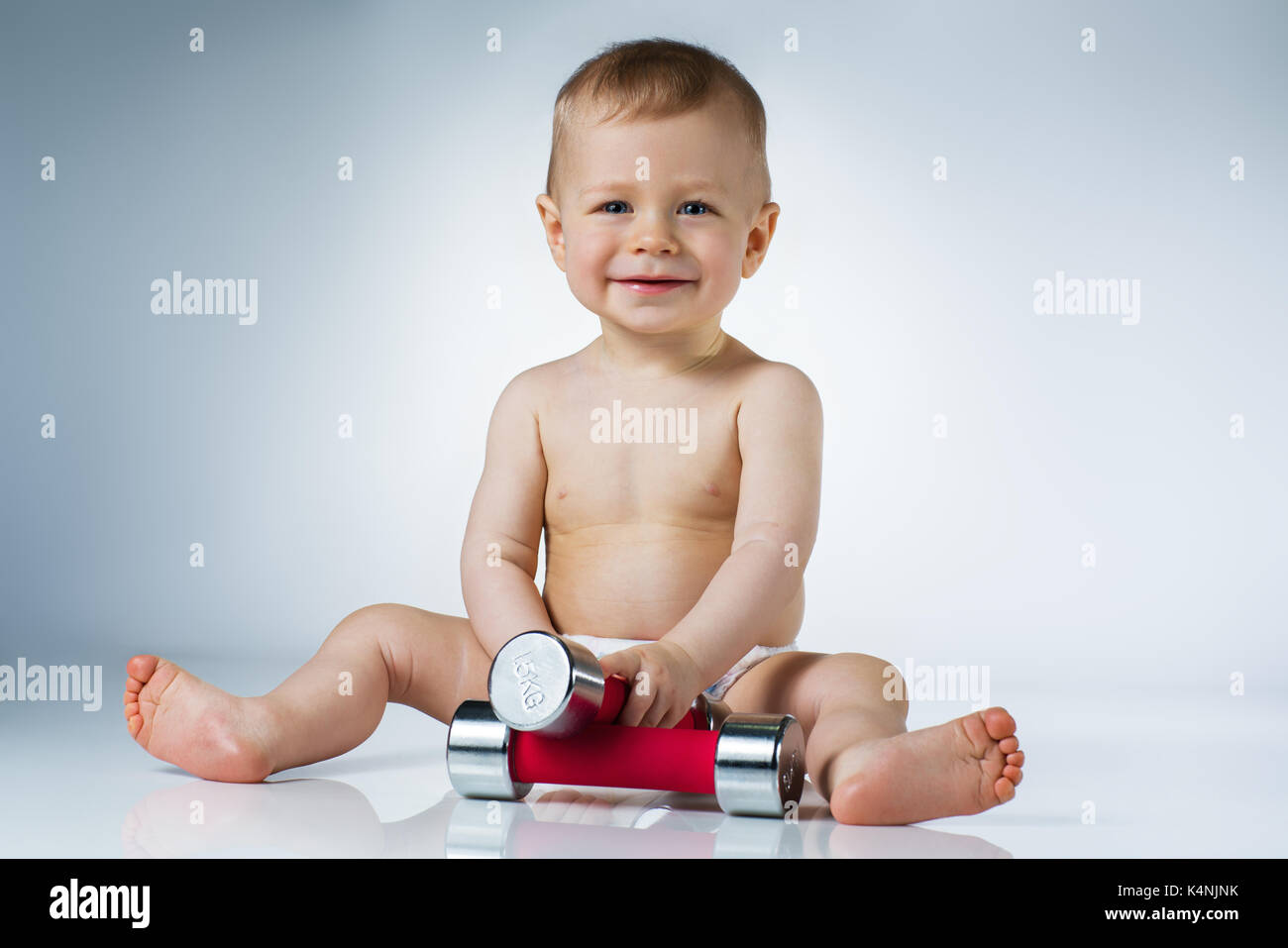 Eight month baby sitting with dumbbells and smiling on white background Stock Photo