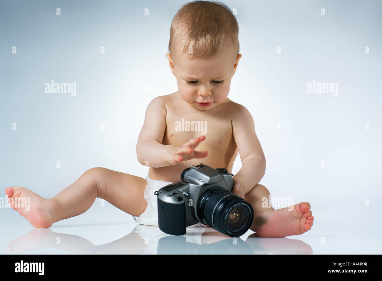 Eight month baby sitting and playing with camera on white background